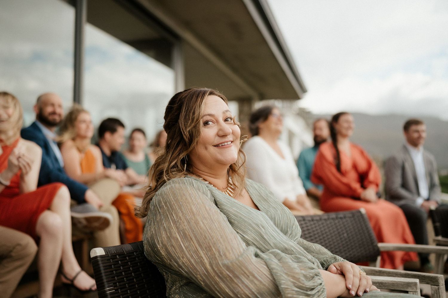 Wedding guests gather outdoors on a cloudy day watching a ceremony unfold.