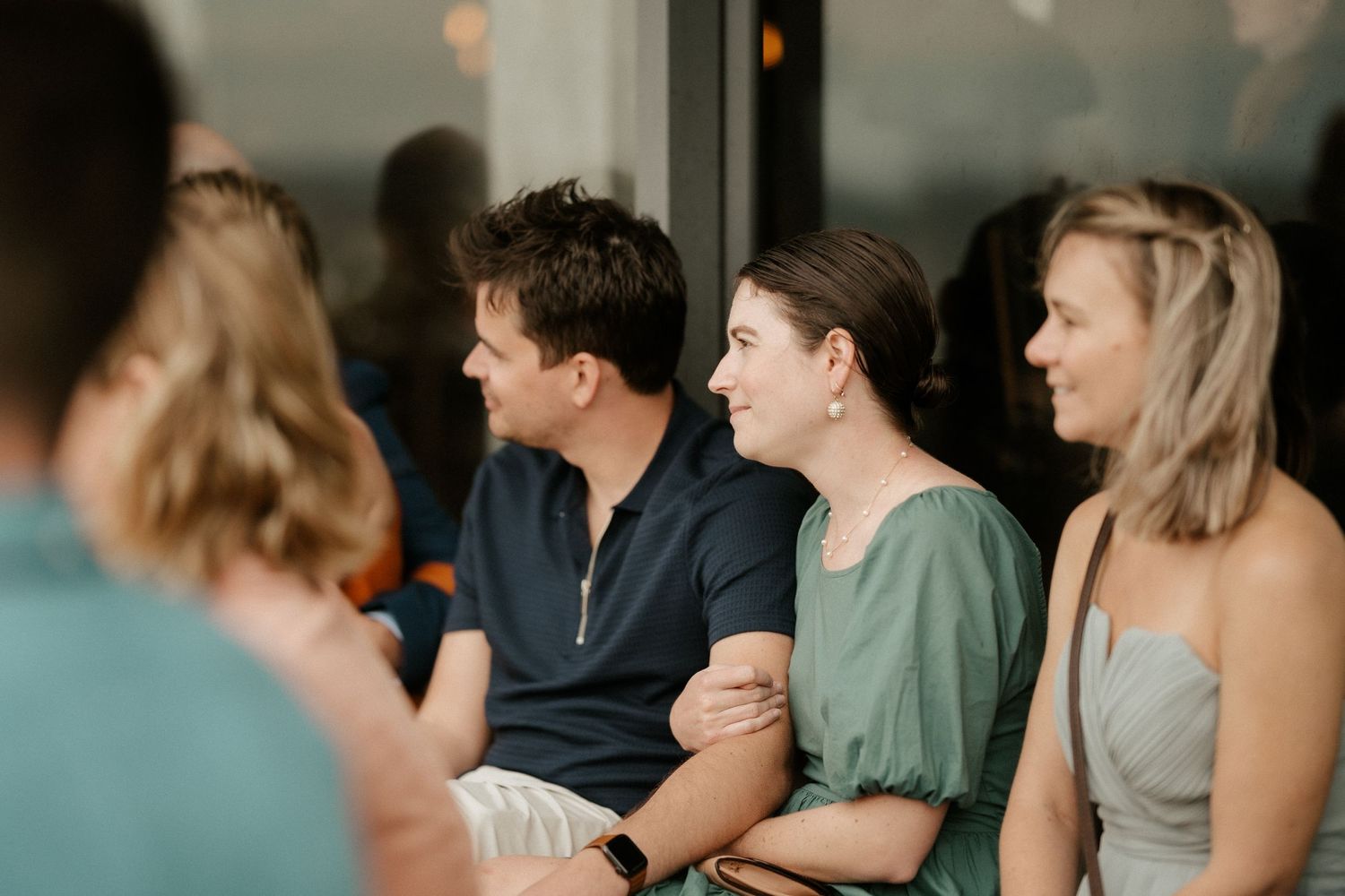 People sitting together at a gathering engaged in conversation with warm lighting in the background.