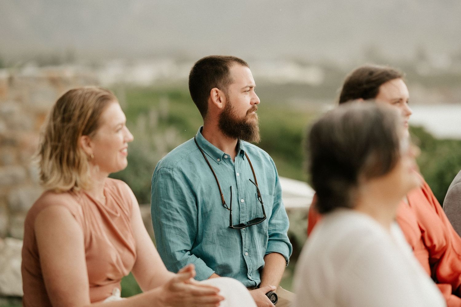 A group of guests gather outdoors during a wedding ceremony with mountain views in the background.