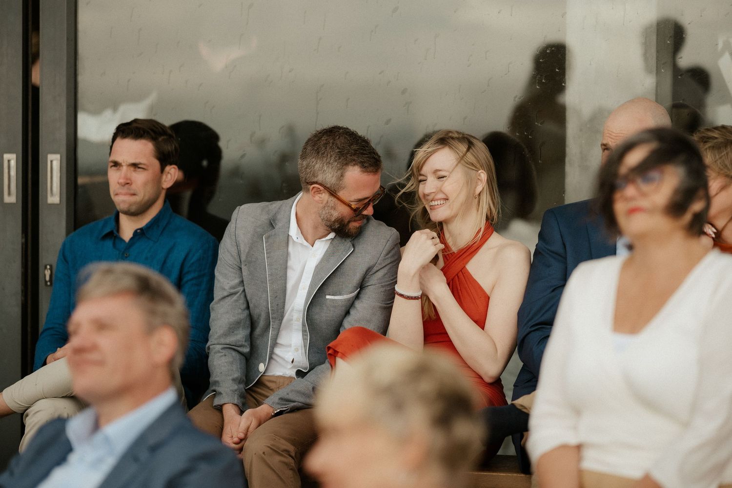 Wedding guests in formal attire sit and share a light moment together.