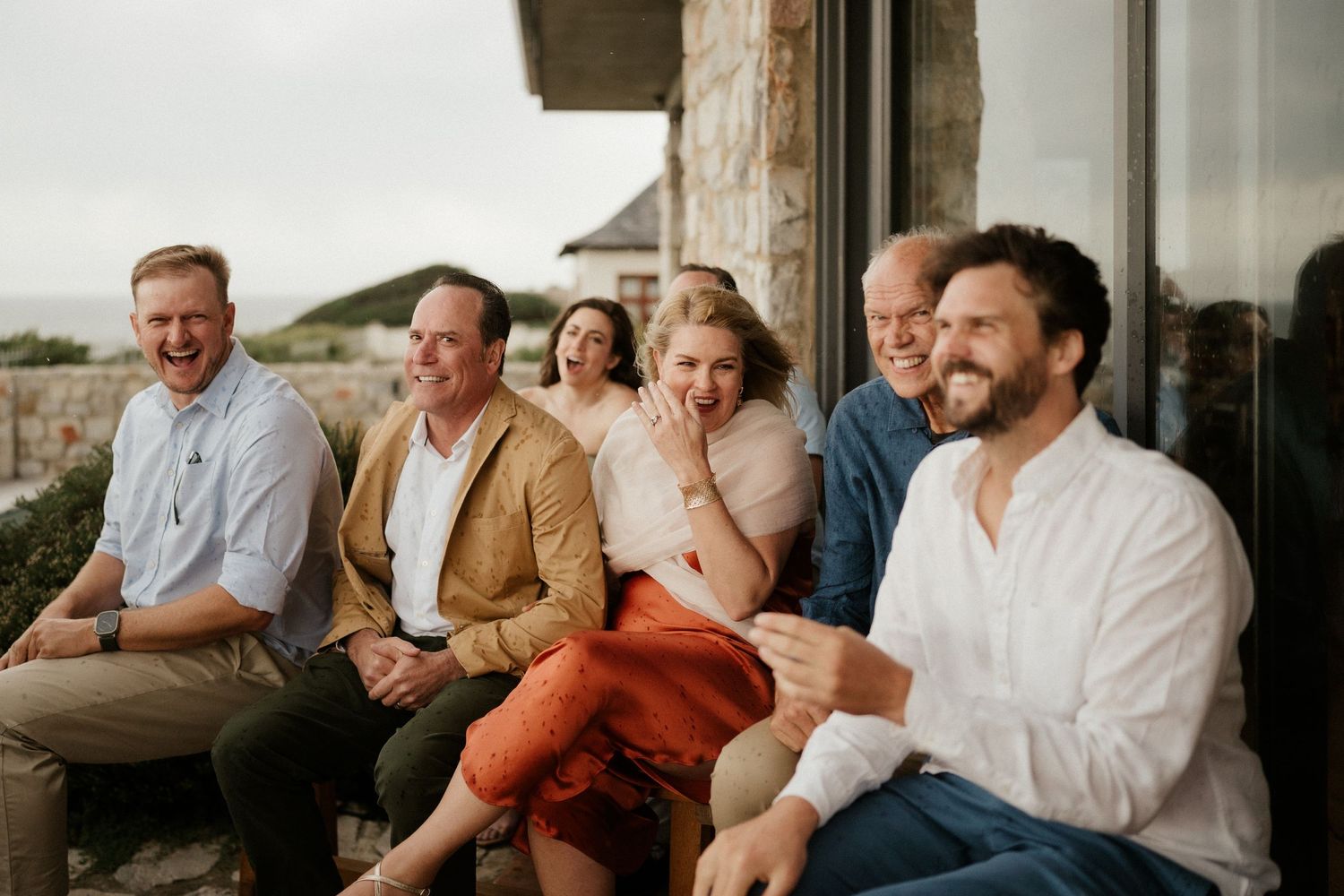 A group of friends laughing together while sitting outdoors at sunset.