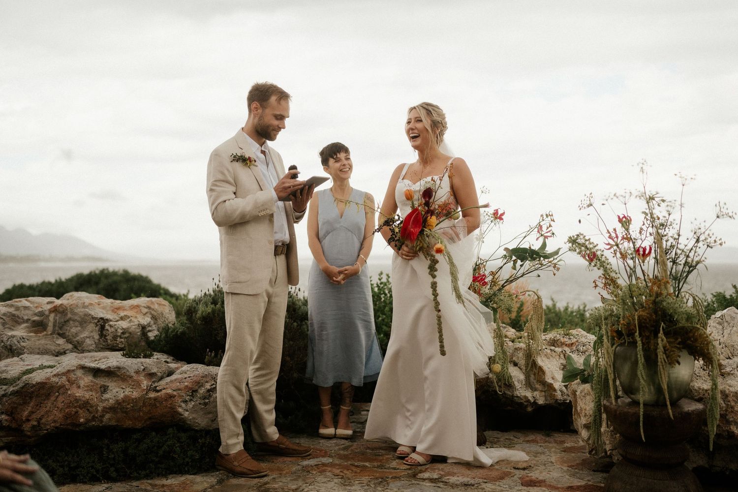An intimate outdoor wedding ceremony takes place on rocky terrain with mountain views.