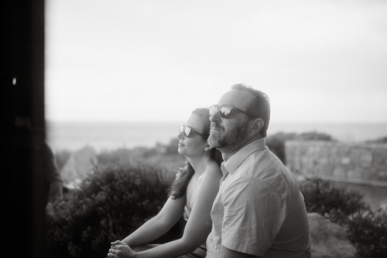 A black and white photograph captures two people gazing at a scenic mountain vista.