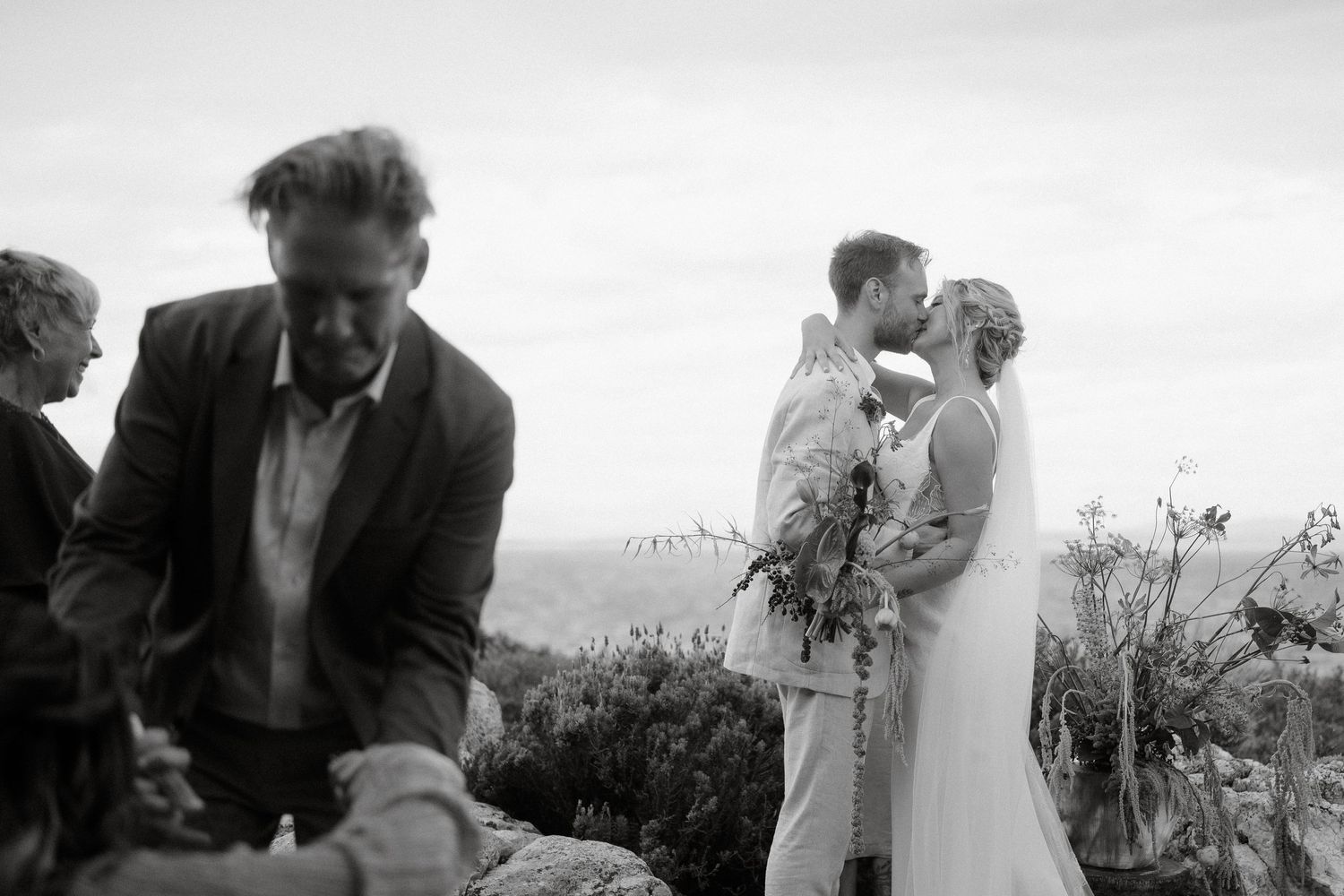 Black and white wedding photograph showing a tender moment between newlyweds in an outdoor setting.