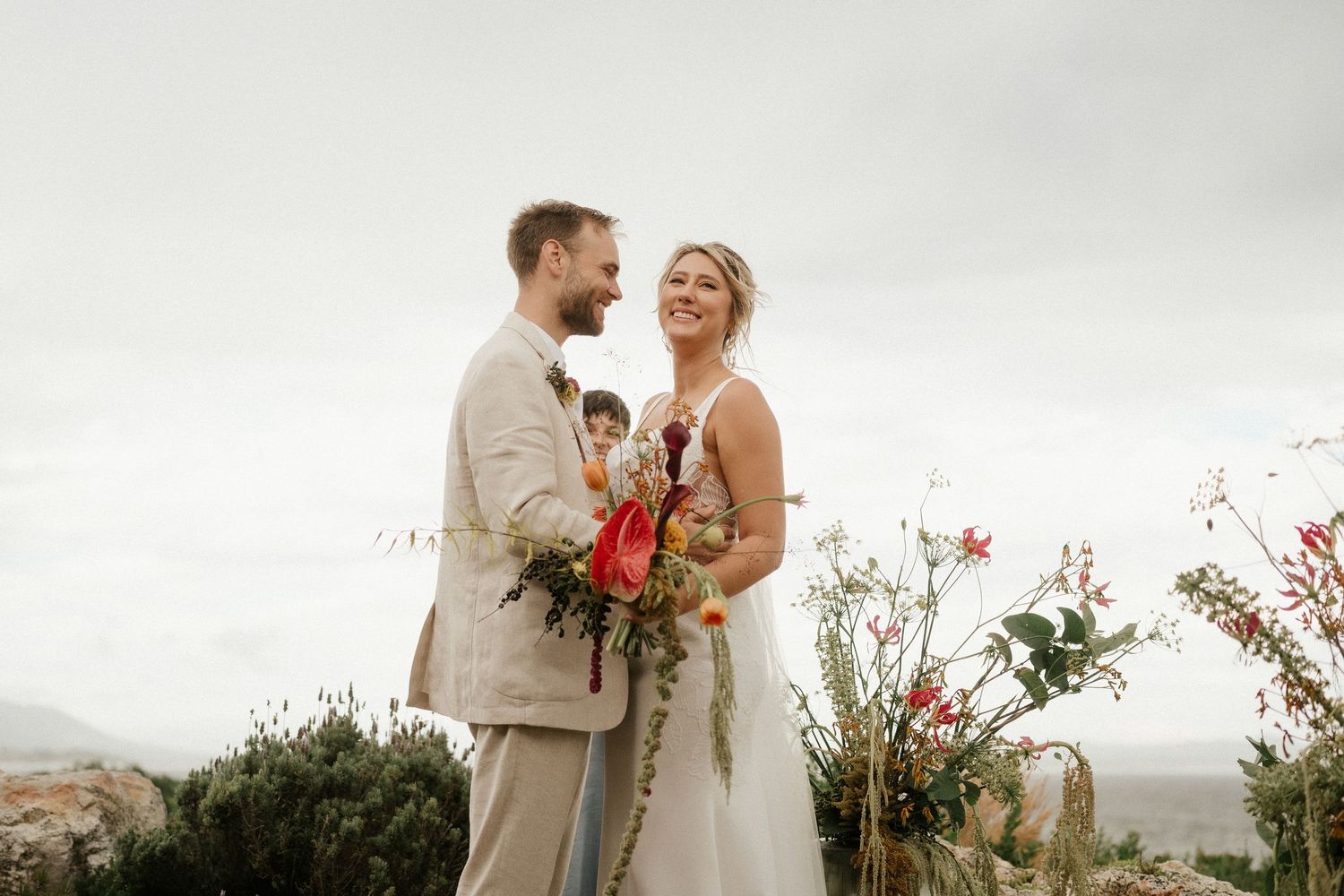 A couple shares a happy moment during their outdoor wedding ceremony with red floral arrangements.