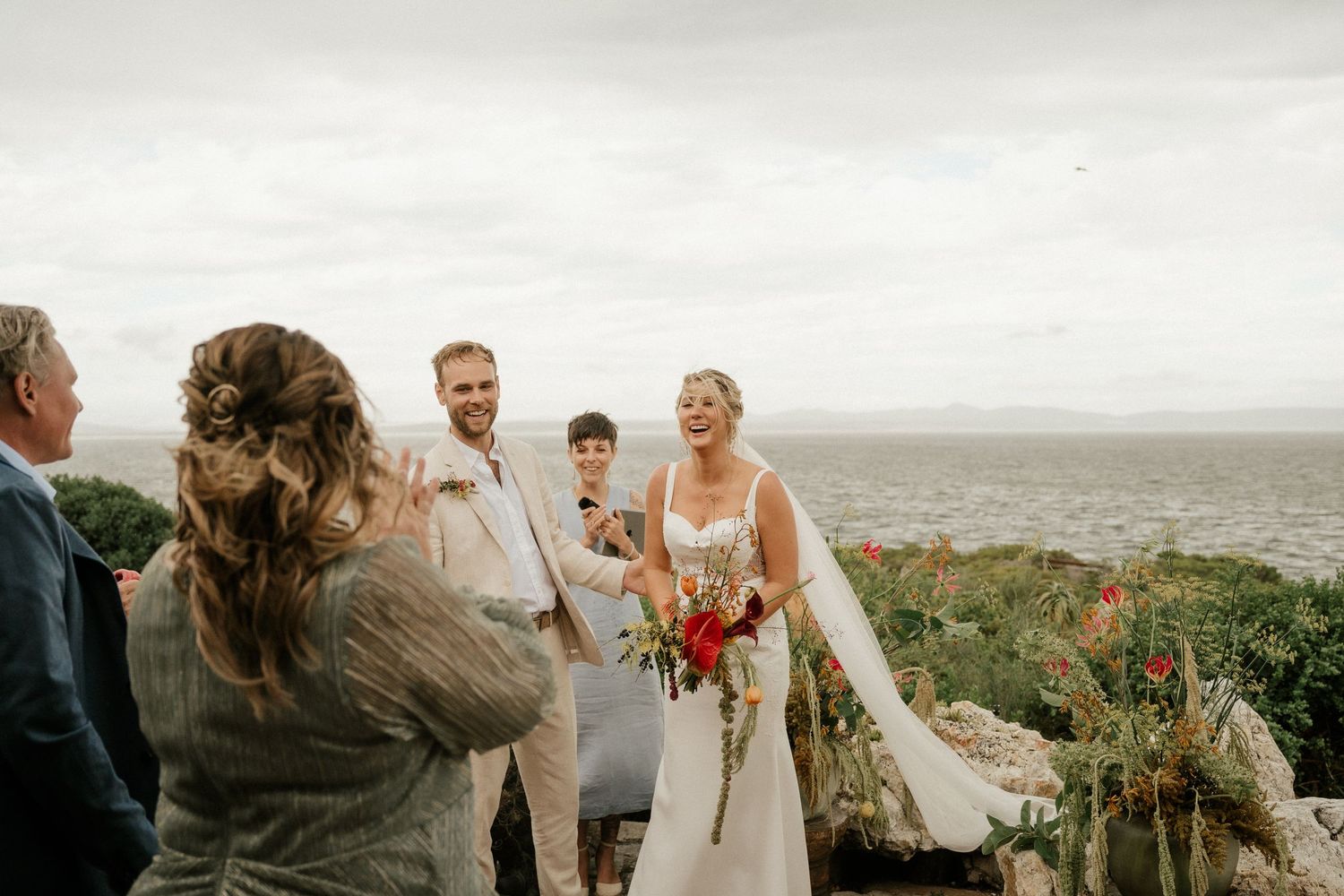 A wedding ceremony takes place on a scenic clifftop overlooking a vast landscape.