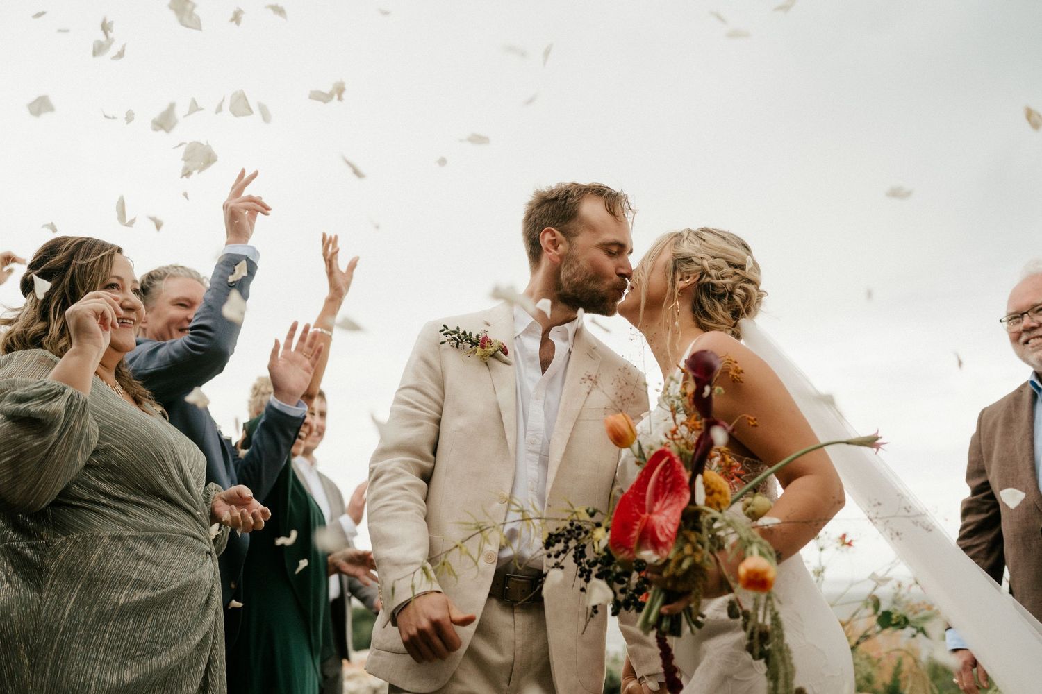 Wedding guests throw confetti as newlyweds share a joyful moment during outdoor celebration.
