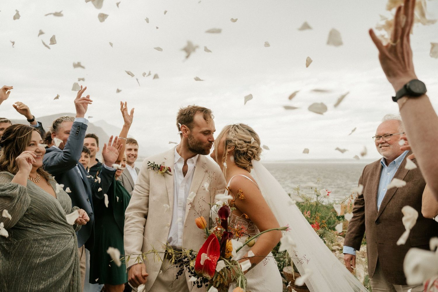 Guests throw confetti as newlyweds celebrate during their outdoor wedding ceremony with mountain views.