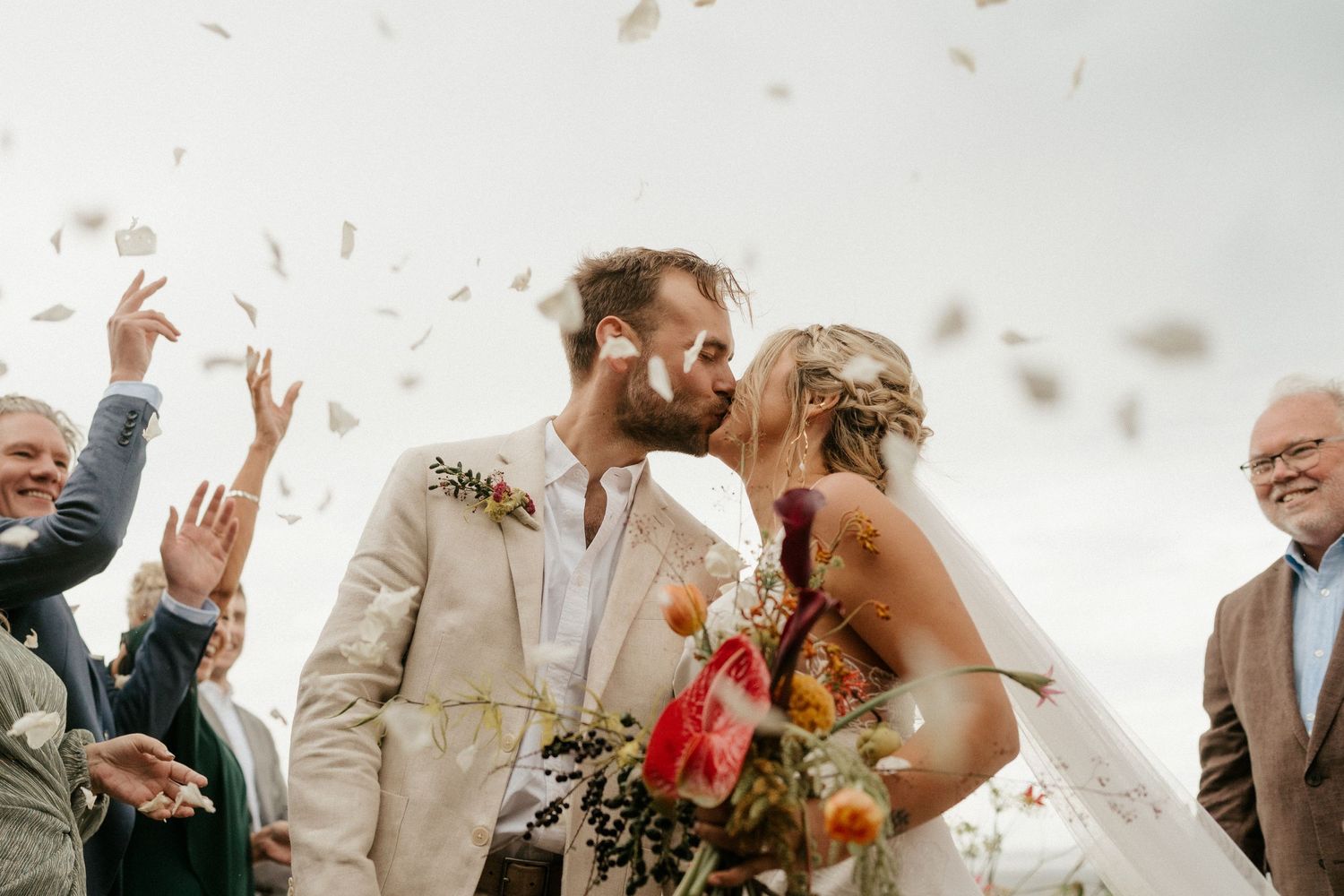 A joyous wedding celebration moment captured with confetti being thrown into the air against a cloudy sky.
