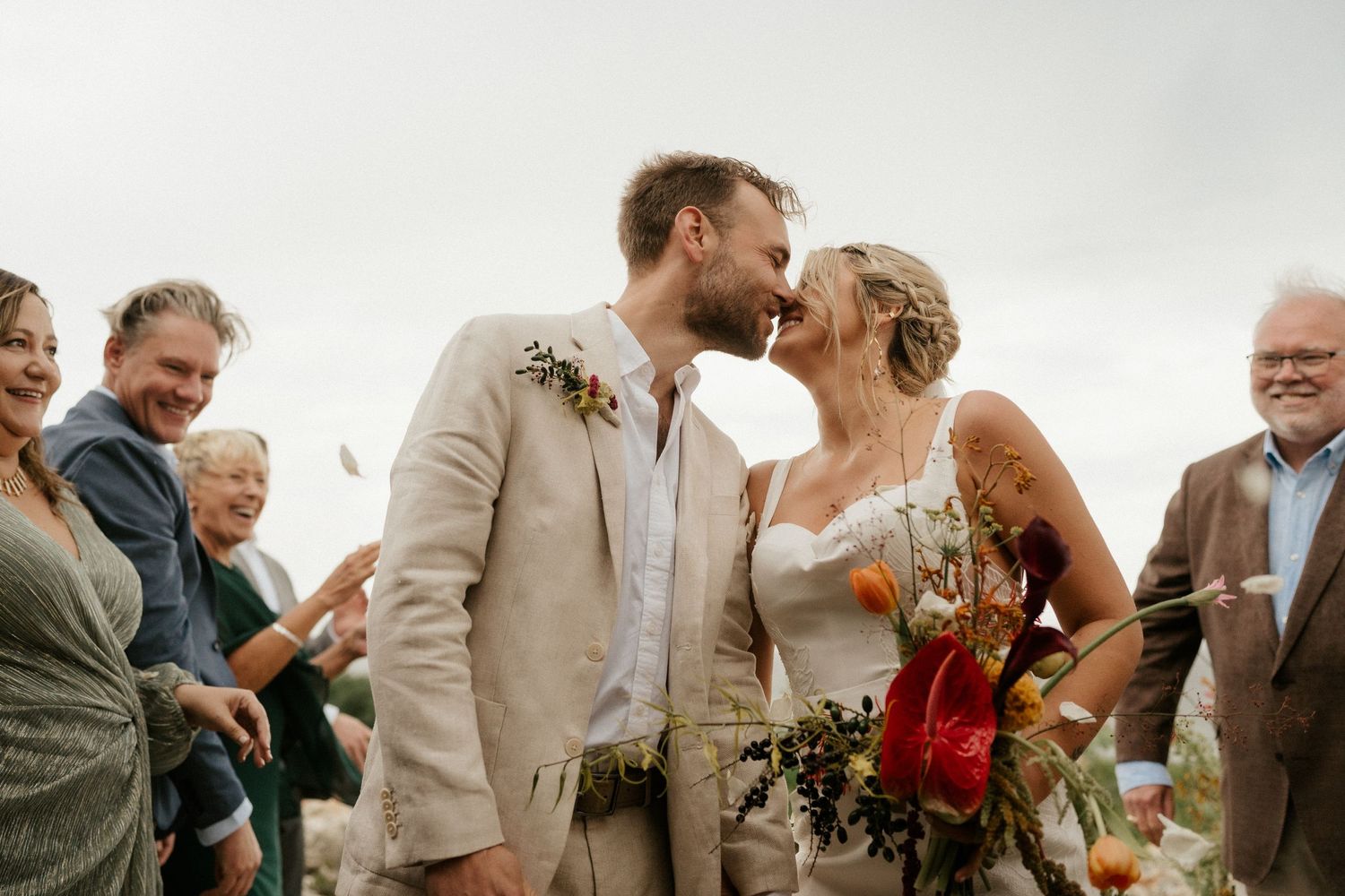 A joyous wedding celebration outdoors with guests looking on as a couple shares a tender moment.