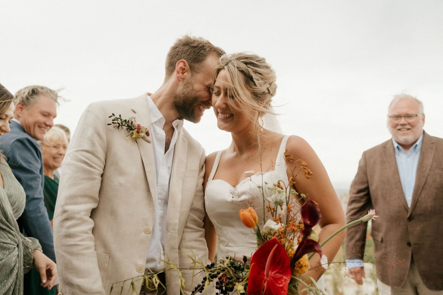 A romantic outdoor wedding moment with a couple embracing while guests look on during a coastal celebration.