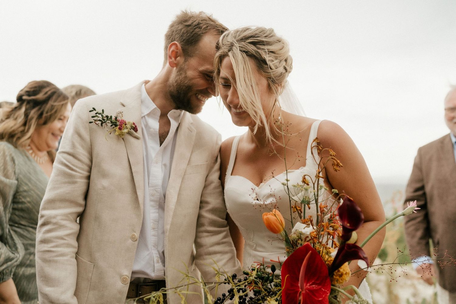 Newlyweds share an intimate moment surrounded by wedding guests during an outdoor celebration.