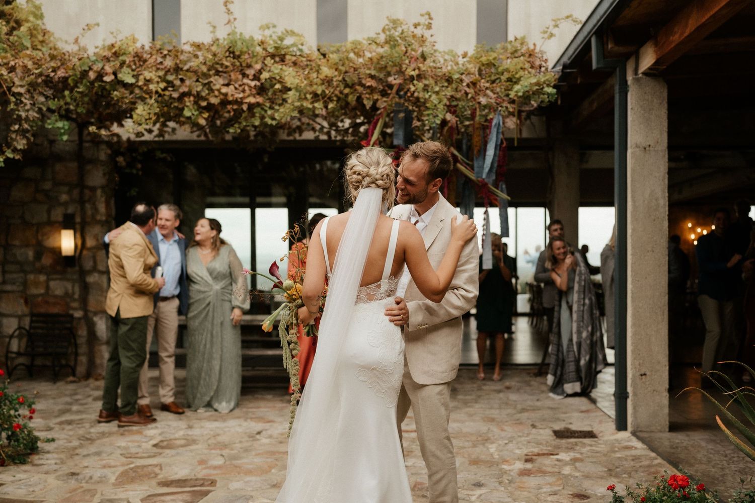 Couple shares their first dance at an elegant outdoor venue decorated with climbing vines and string lights.