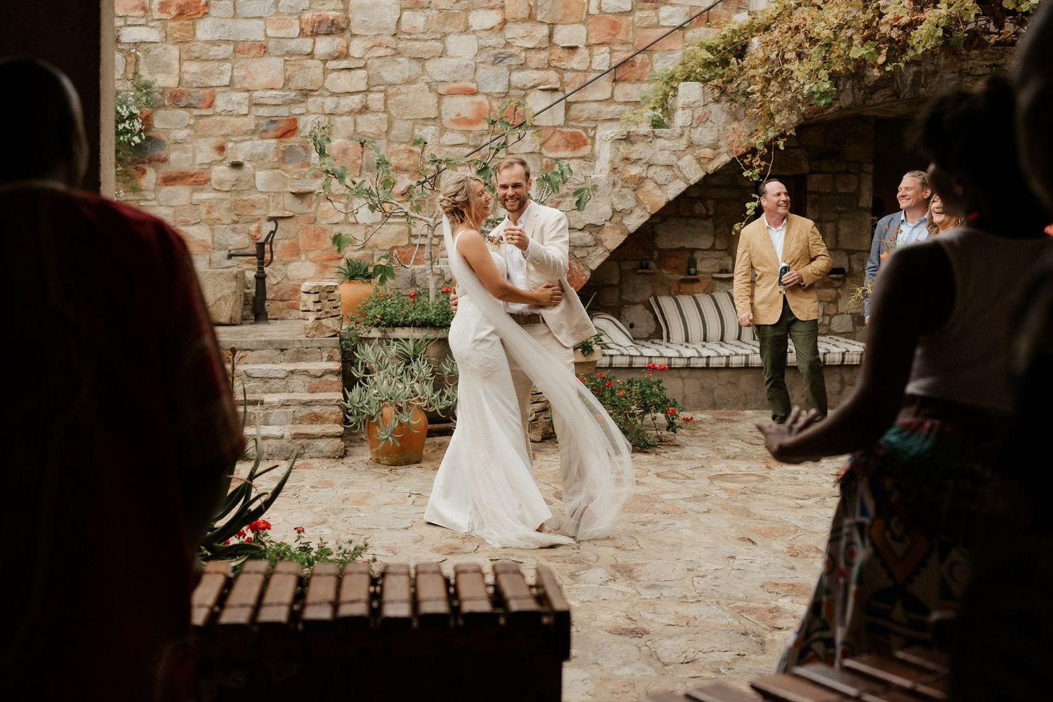 A romantic wedding ceremony takes place in a rustic stone courtyard at sunset.