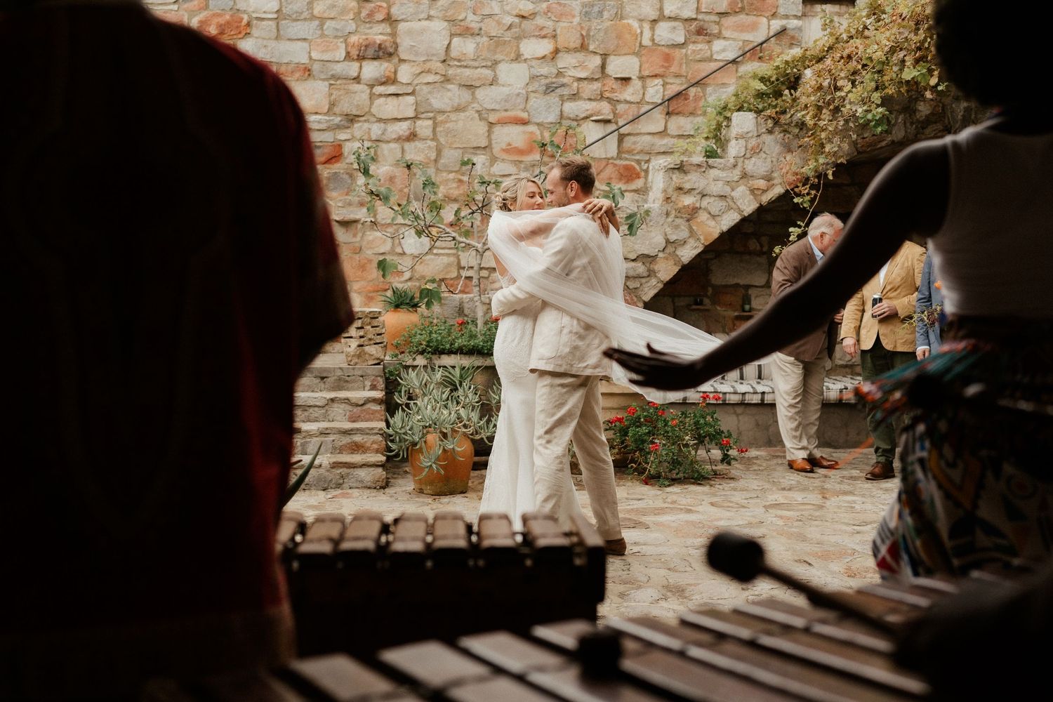A couple dances together in a rustic stone courtyard as fabric flows in the wind.