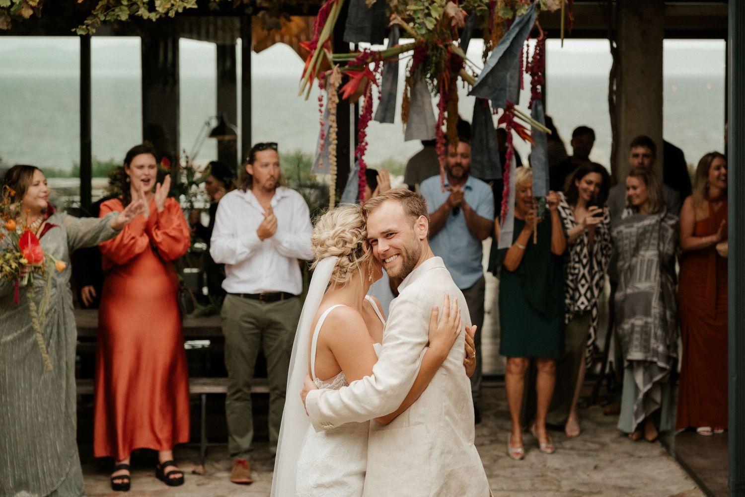 Wedding guests applaud and celebrate as a couple shares their first dance under decorative lighting.