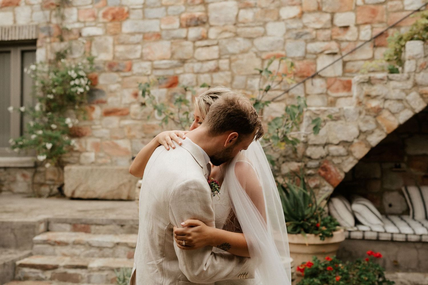 Romantic moment between newlyweds against rustic stone wall with climbing vines.