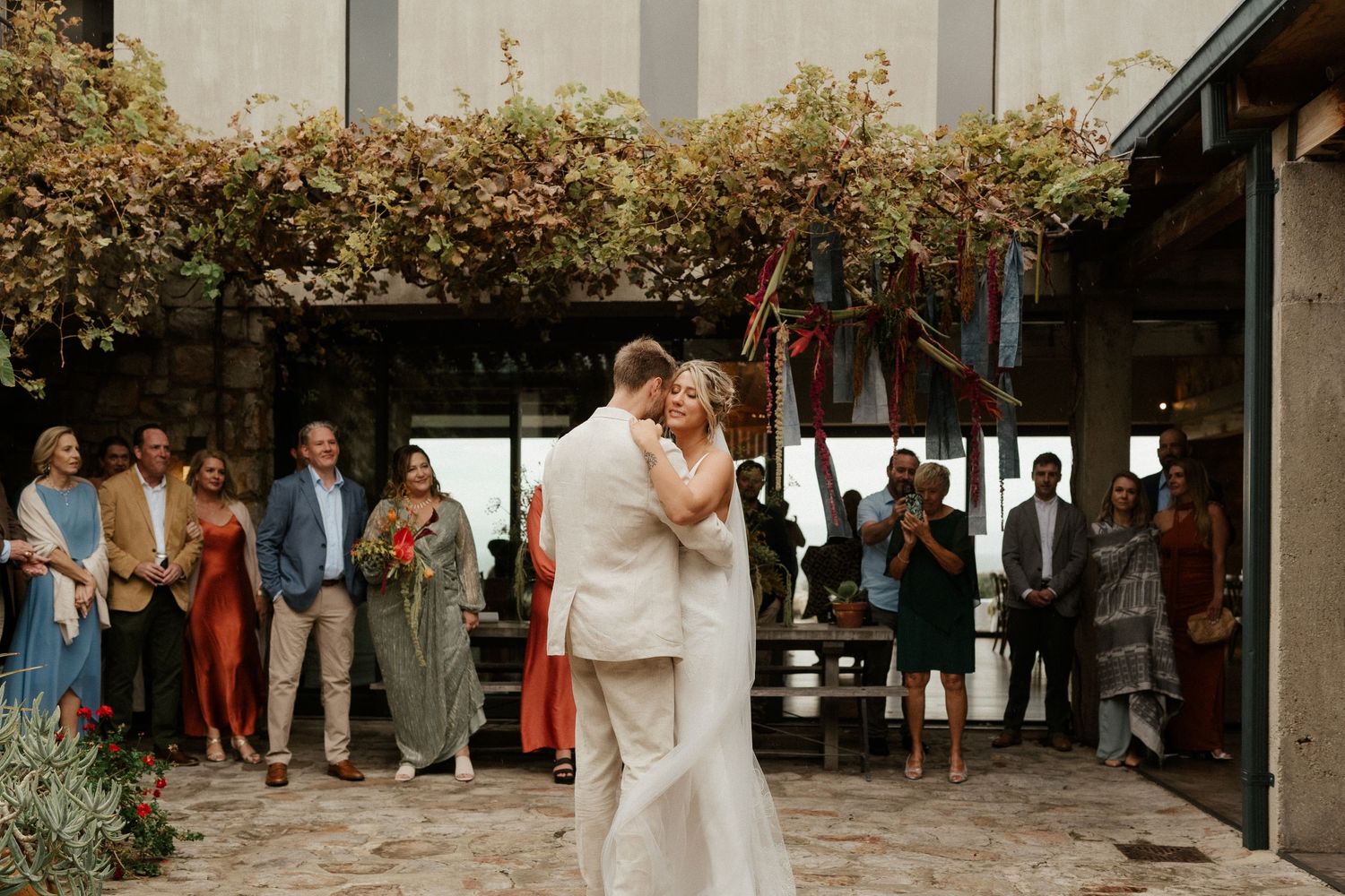 A couple shares a romantic slow dance at an intimate outdoor wedding reception with guests watching.