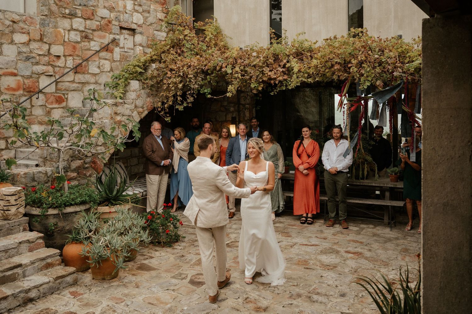 Couple shares their first dance in a rustic courtyard surrounded by stone walls and climbing vines.