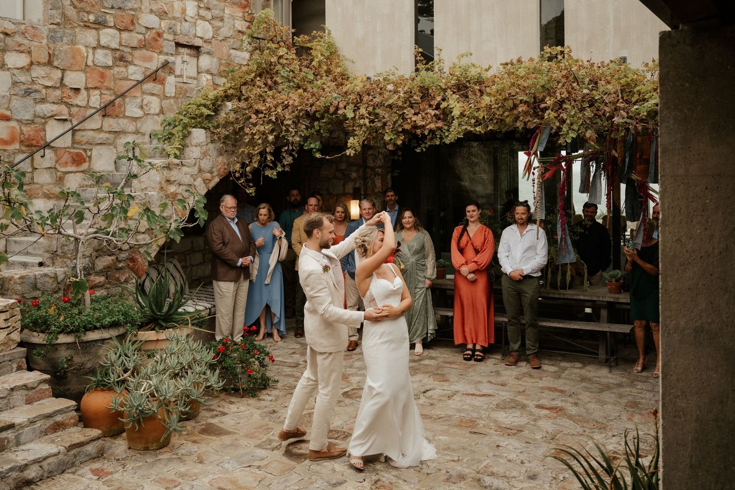 A couple dances intimately in a rustic stone courtyard surrounded by wedding guests.