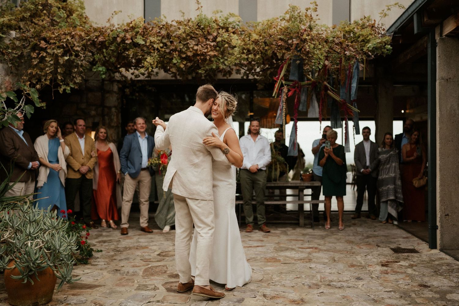 A couple shares their first dance in a charming courtyard with climbing vines and stone walls.