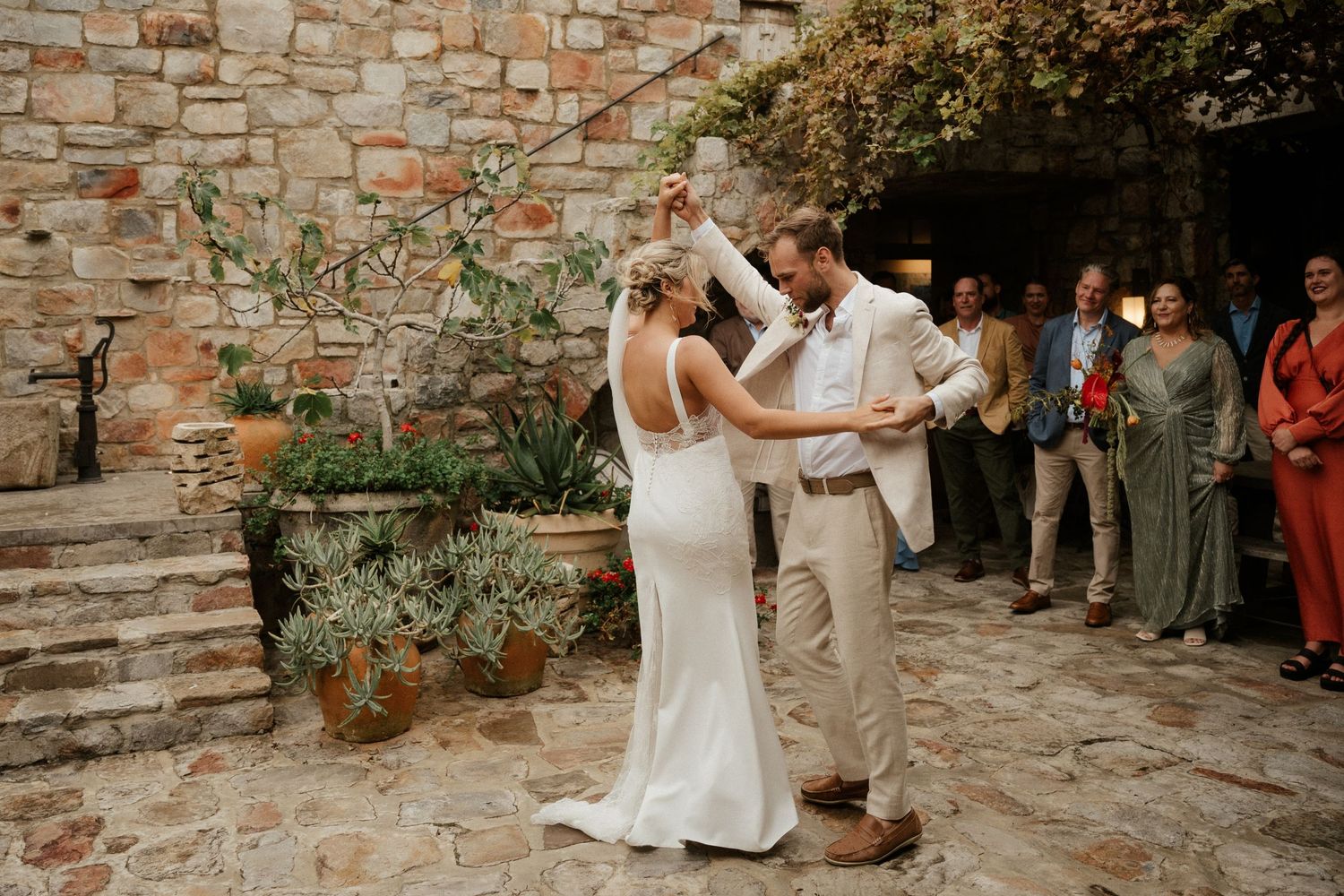 A romantic first dance takes place in a rustic stone courtyard during a wedding celebration.