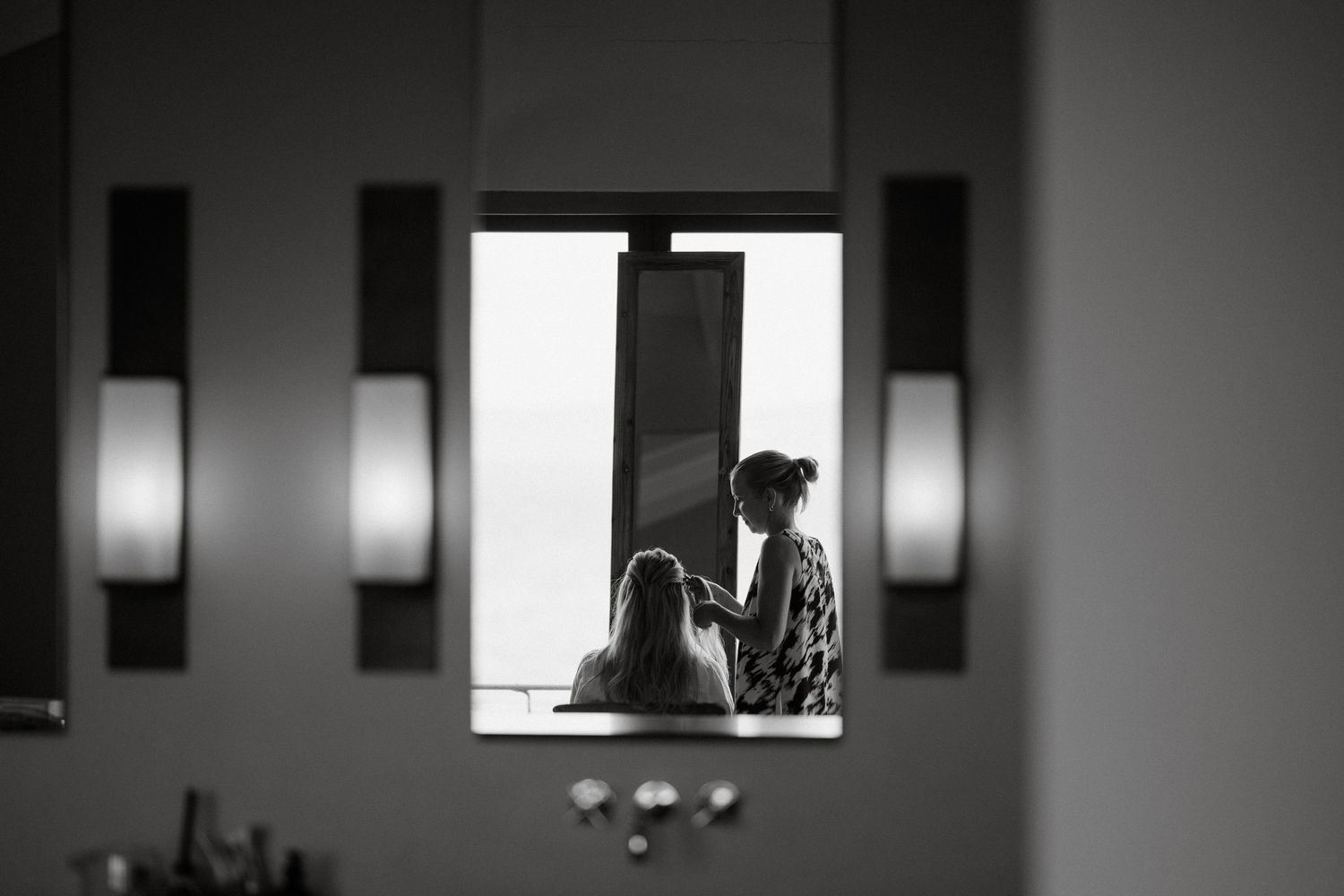 A black and white silhouette through a window frame with wall sconces visible in the foreground.