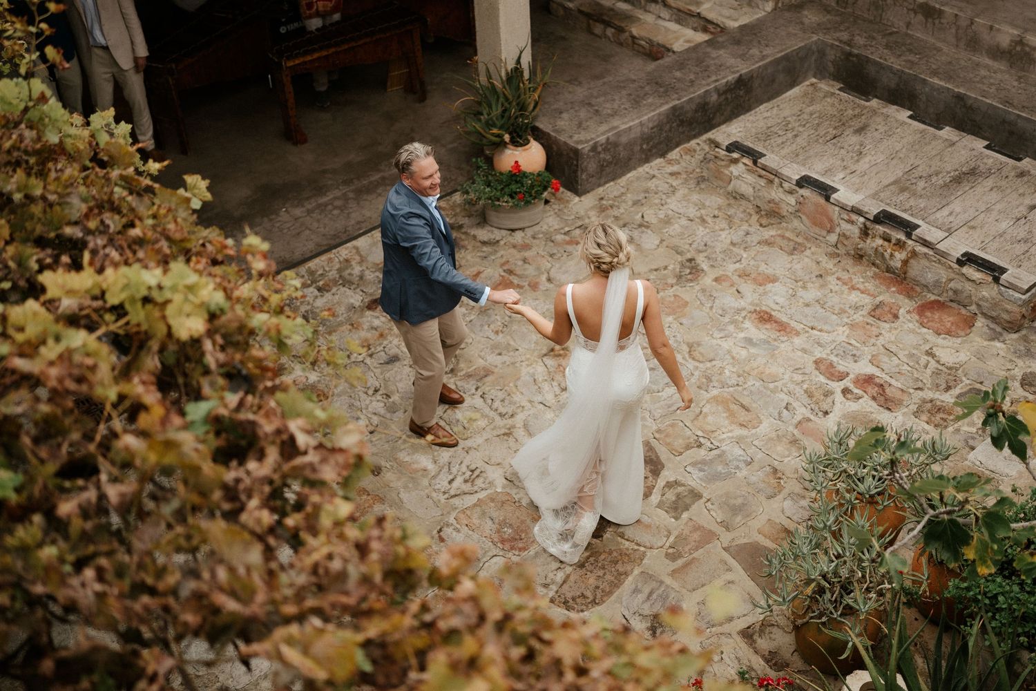 A couple dances together in an outdoor courtyard surrounded by stone walls and greenery.