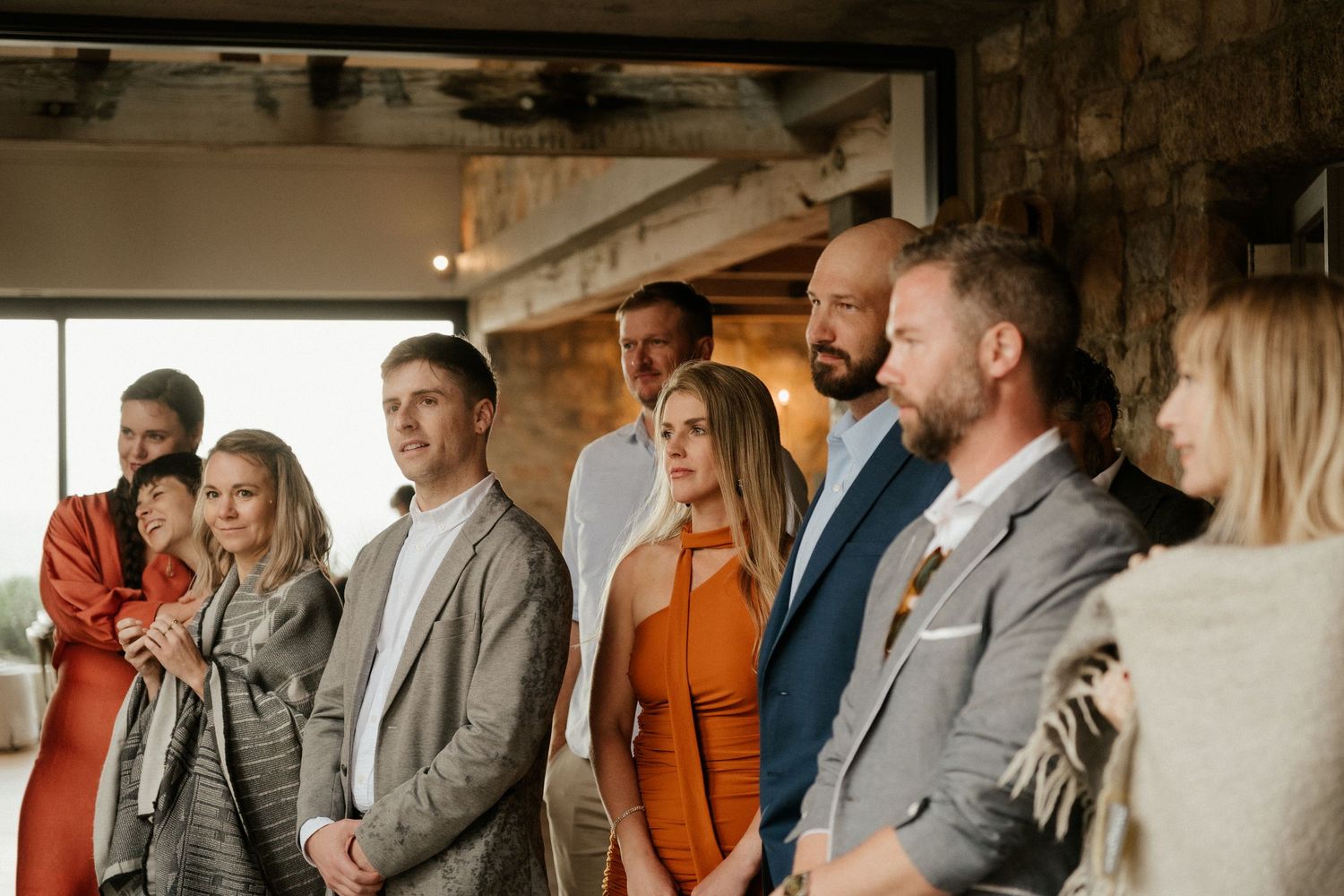 Wedding guests standing in a line wearing formal attire at an indoor venue.