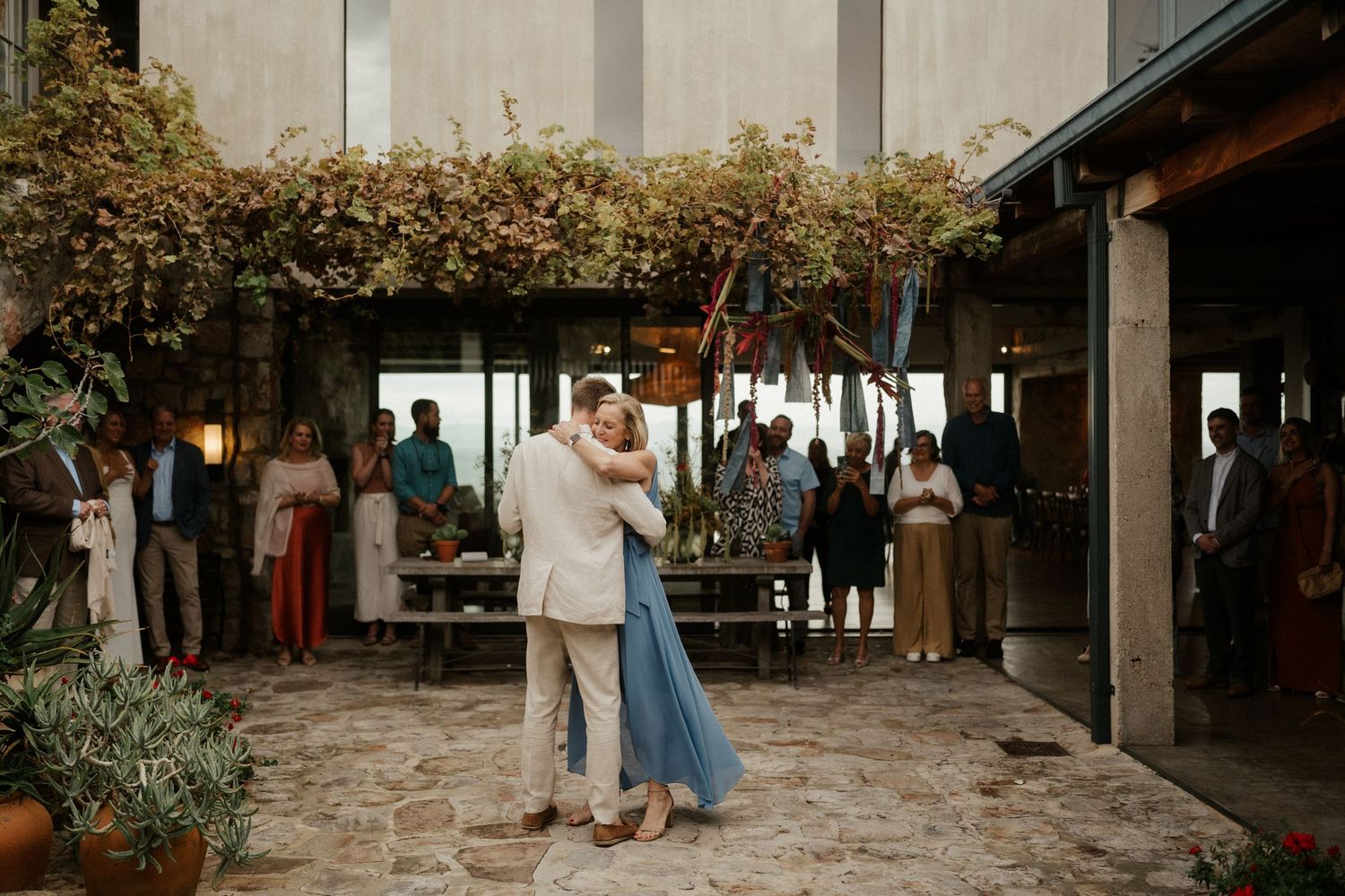 Couple dancing outdoors under hanging greenery and string lights at an evening celebration.