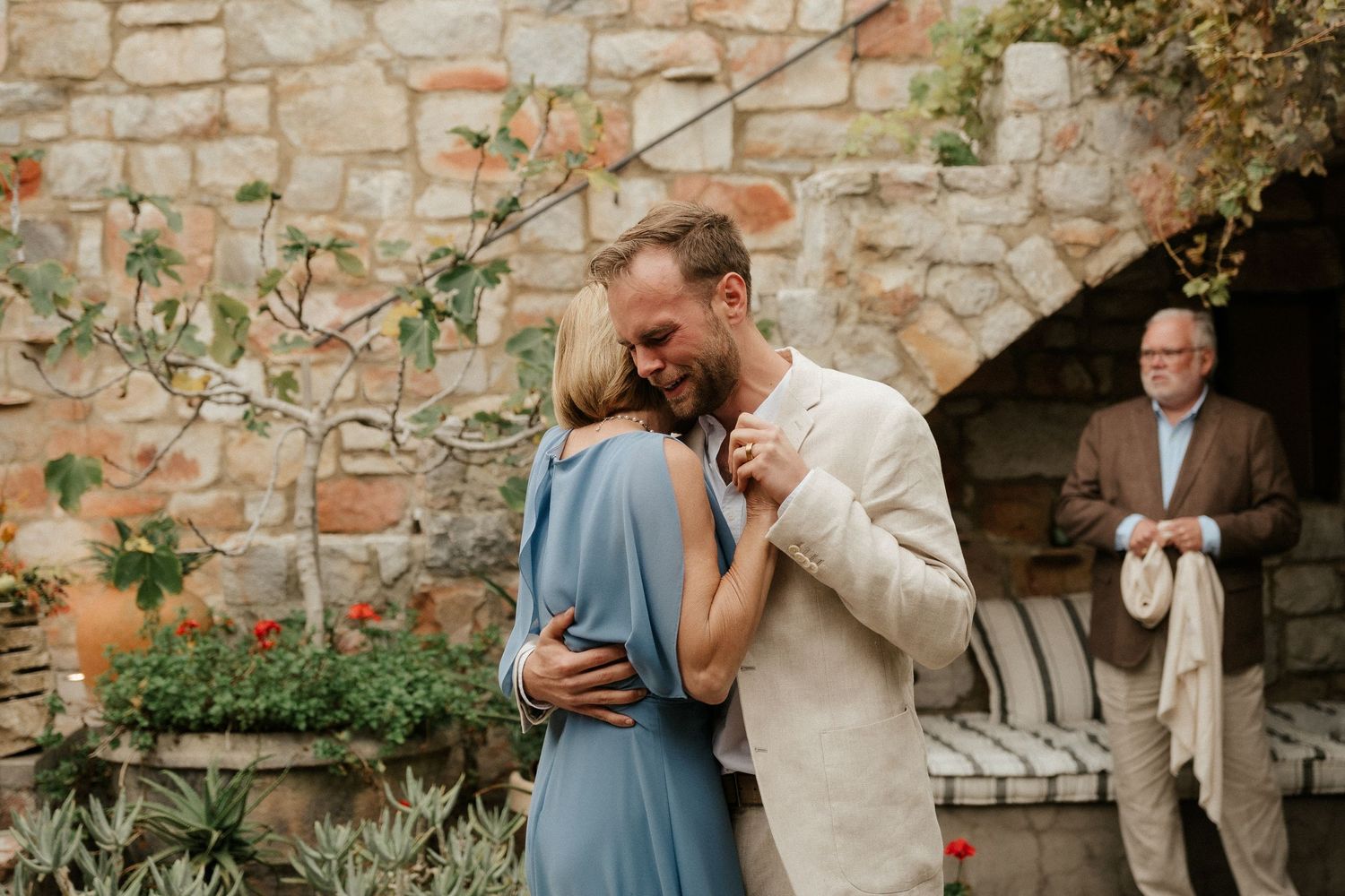 Intimate moment shared in a garden setting with stone wall backdrop.