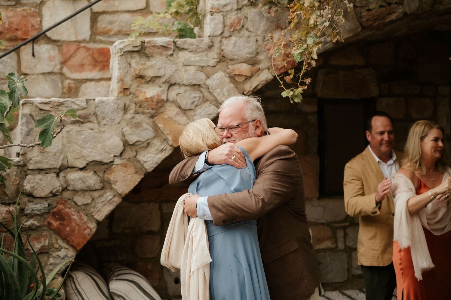 Emotional embrace between attendees at a stone-walled venue during celebration.