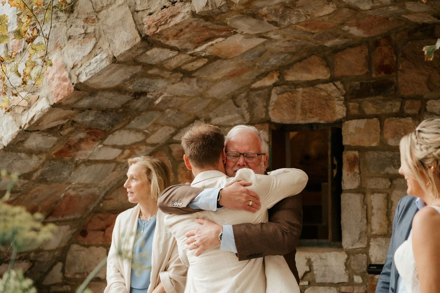 An emotional embrace taking place against a rustic stone wall background.