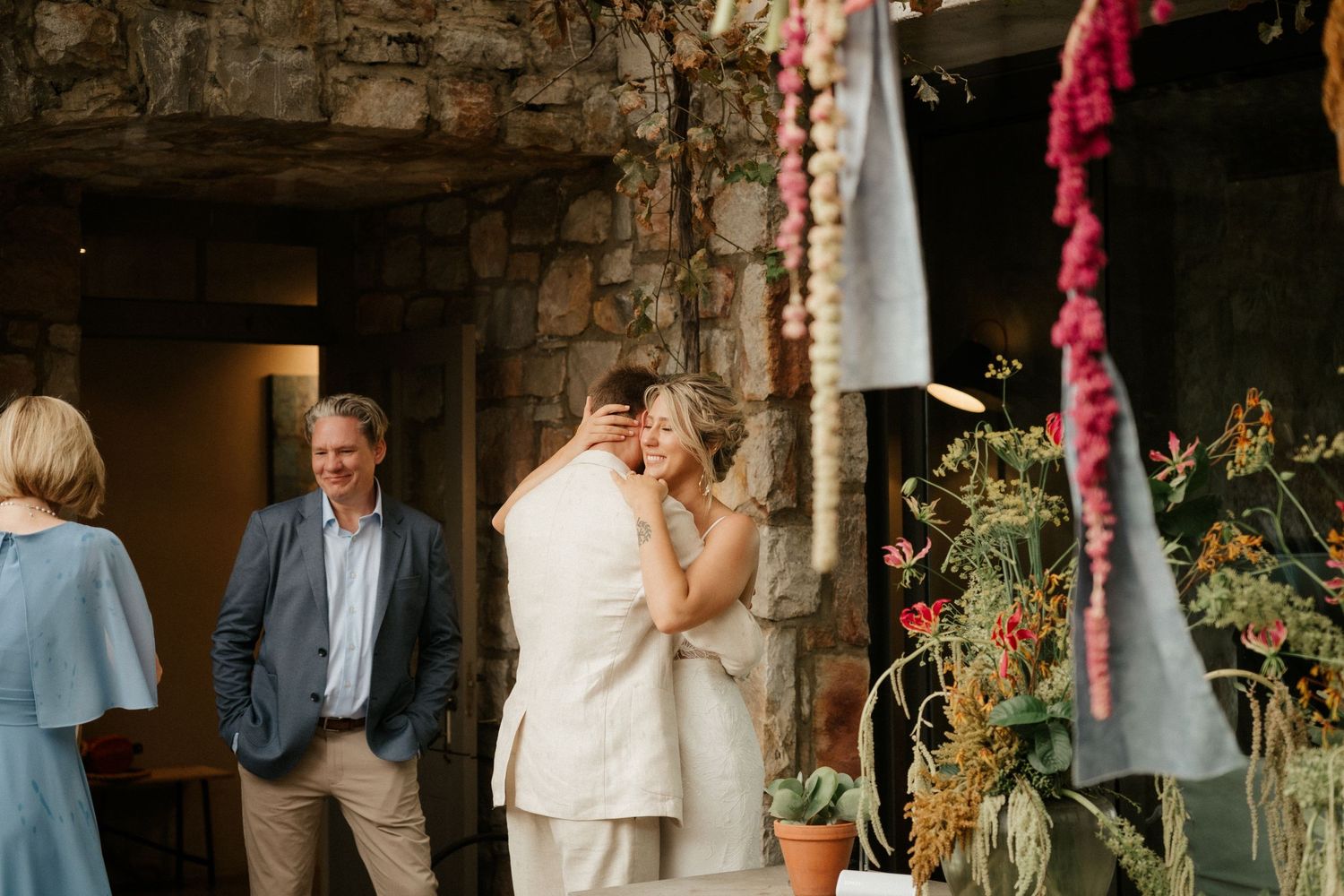 A tender moment shared during an outdoor ceremony with stone walls and floral decorations.