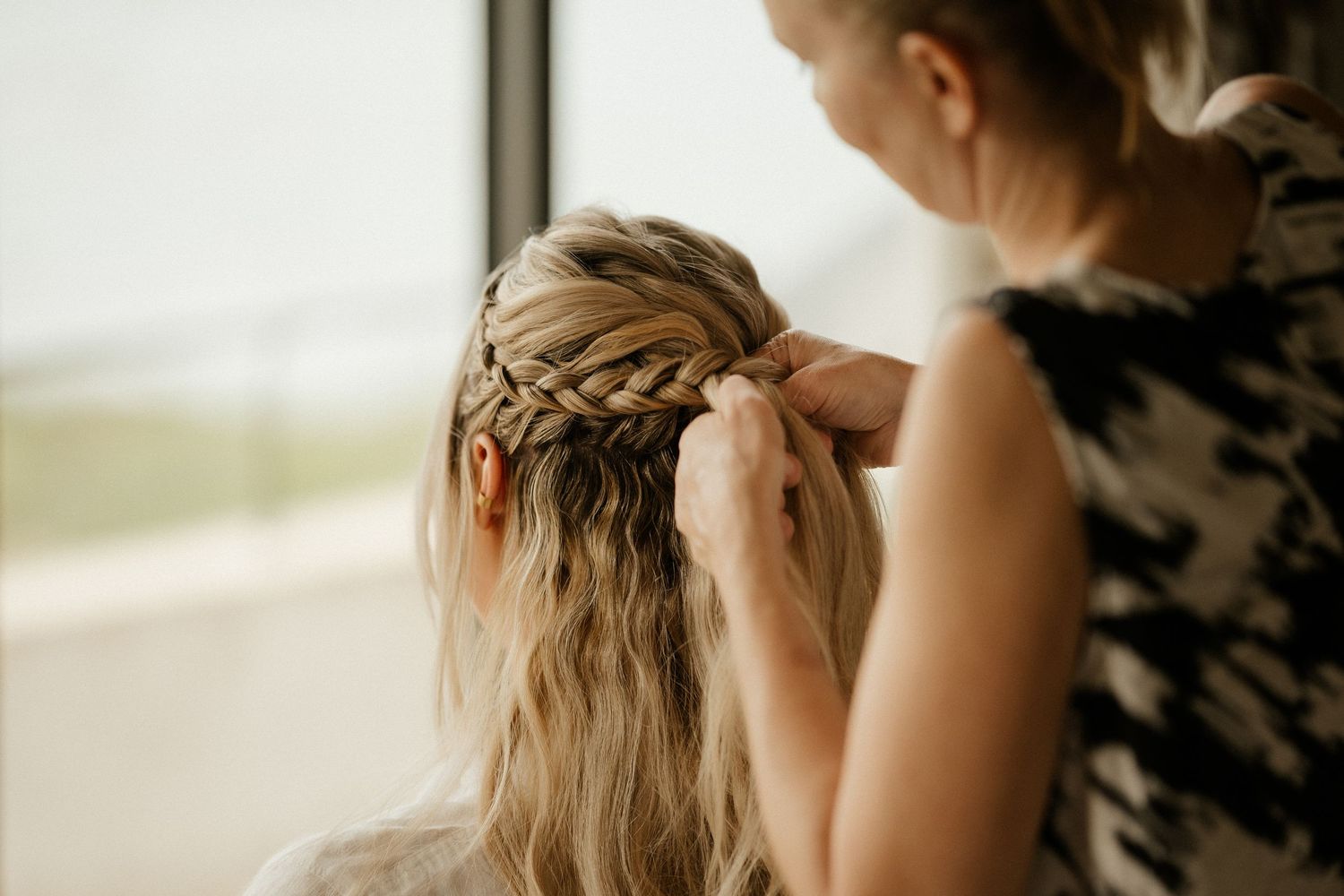Close-up of intricate braided hairstyling being done with blonde hair in natural light.