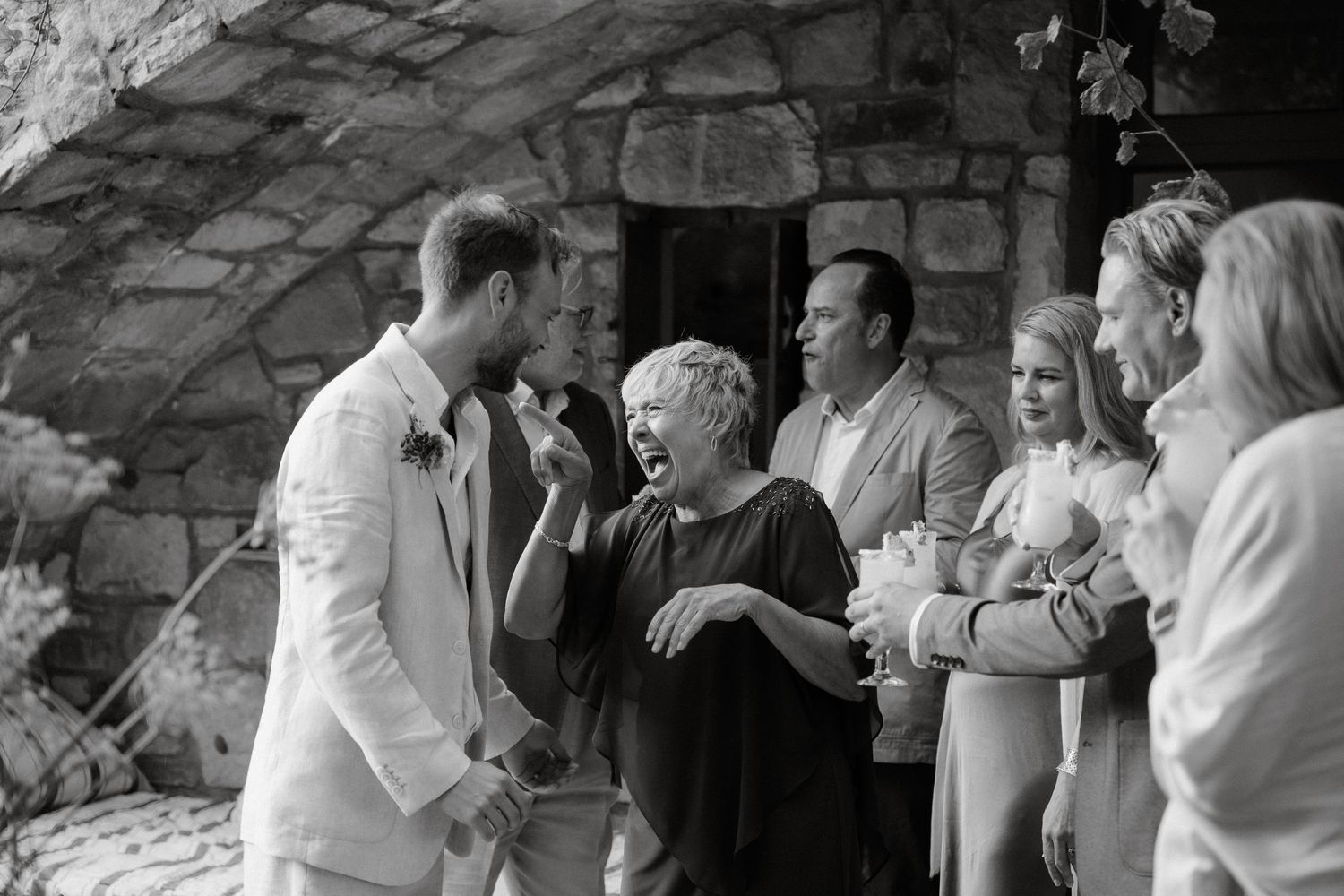 A black and white photo capturing joyful interactions at a stone venue wedding.