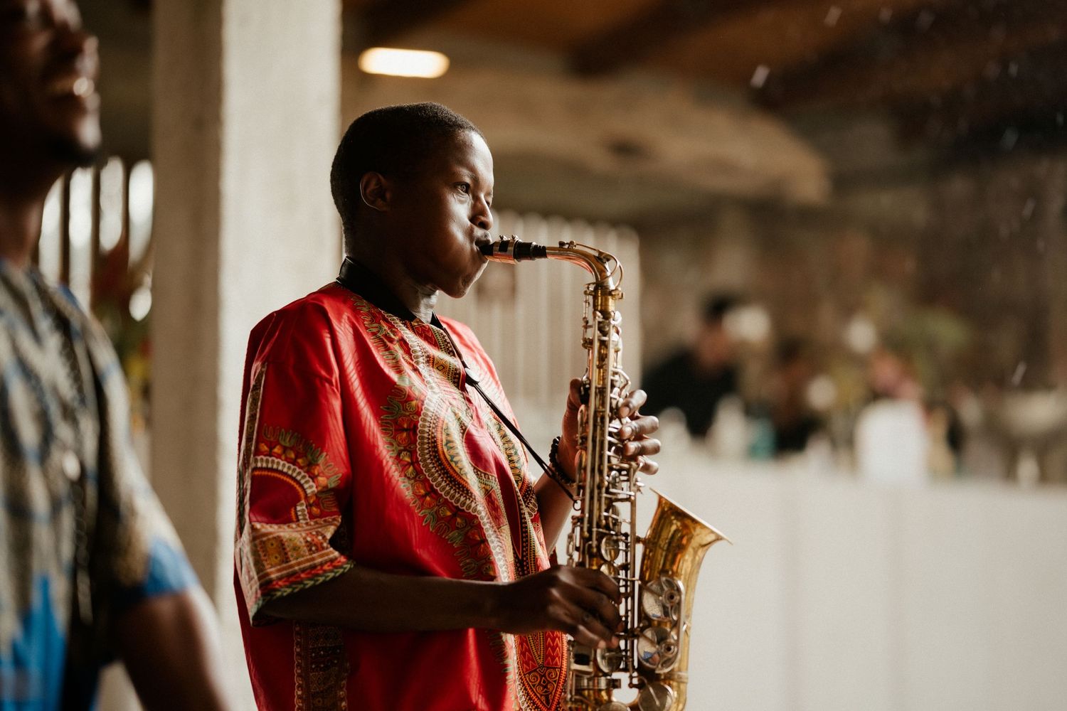 A musician in a red shirt performs on saxophone at an event venue.