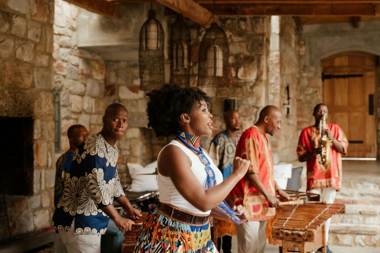 Musicians perform energetically on traditional instruments in a rustic stone room with wooden beams.