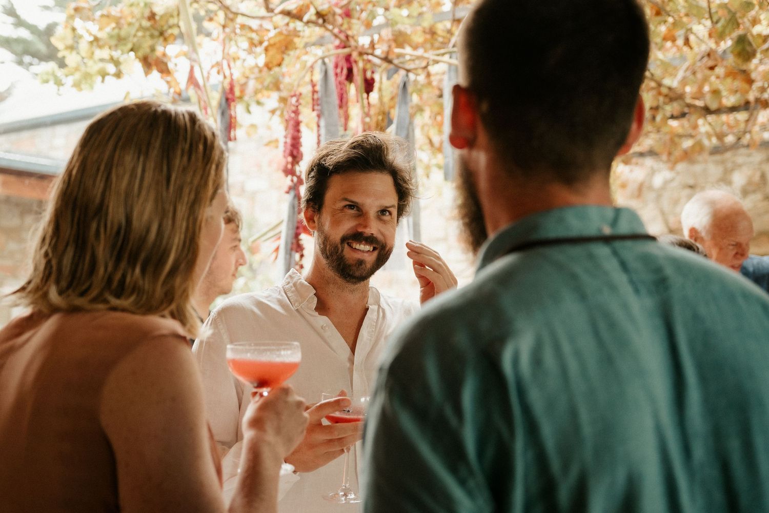 Guests enjoying cocktails under hanging decorations at an outdoor wedding reception.