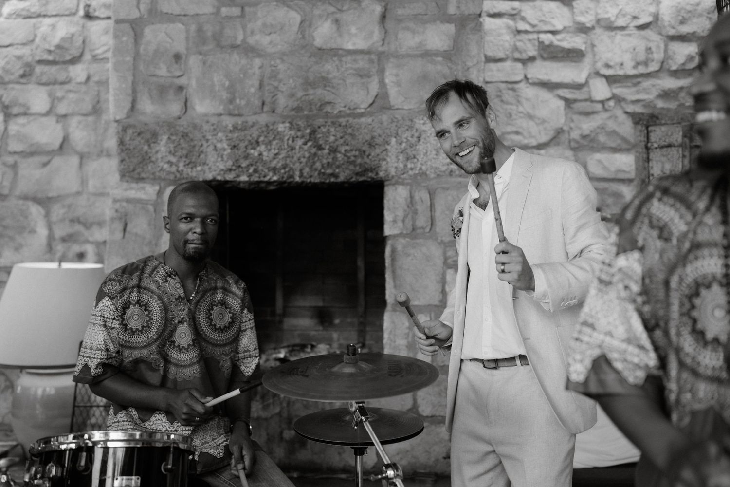 A black and white photo shows musicians performing in a rustic stone room with a fireplace.