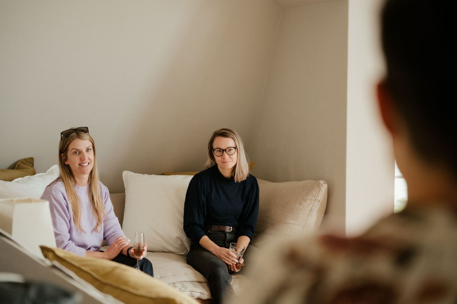 Two individuals sit on a beige couch during what appears to be a therapy or counseling session in a sunlit room.
