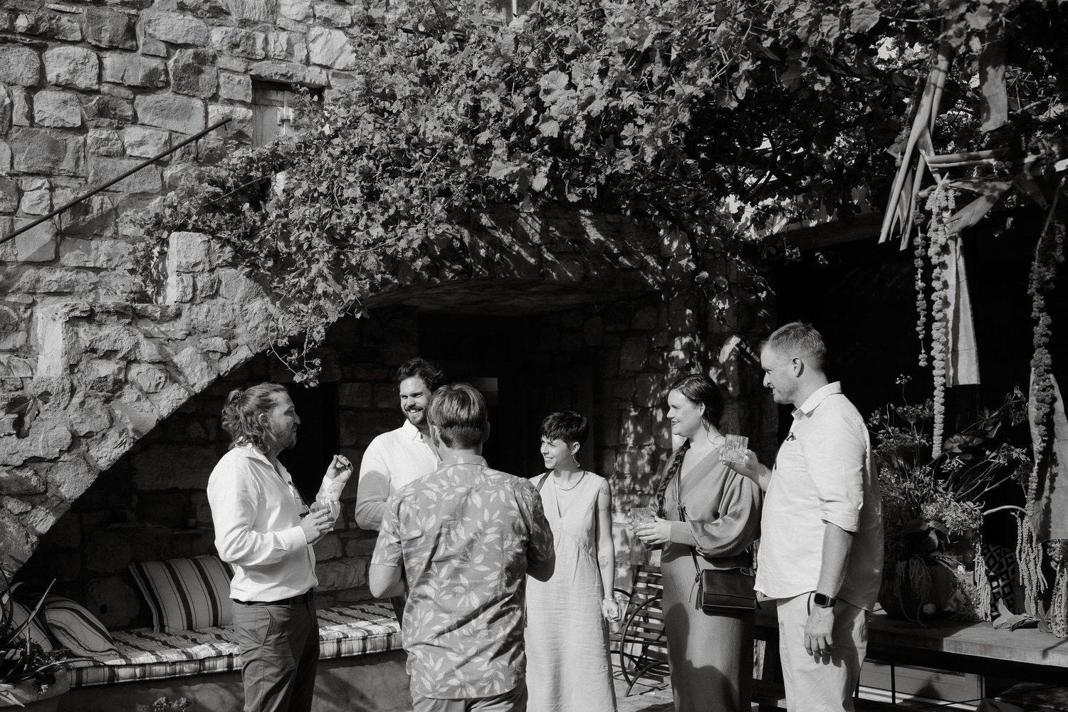 Group gathered for drinks and conversation outdoors near a stone wall.