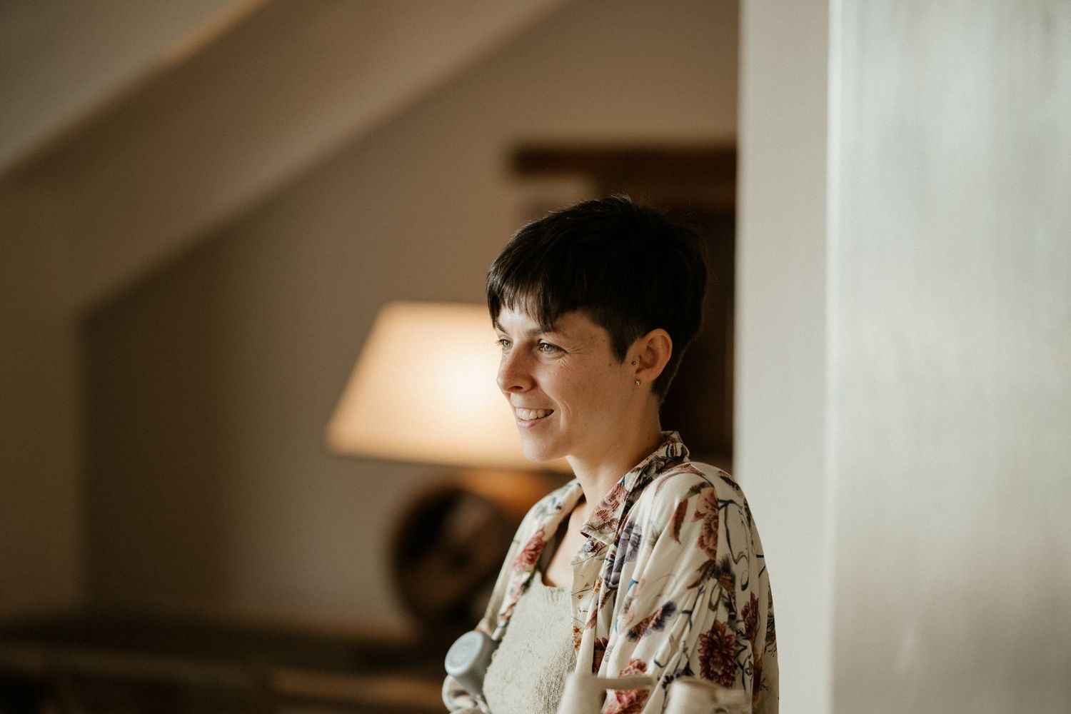 A soft warm-lit portrait showing a person in a floral patterned shirt looking to the side with a gentle expression.