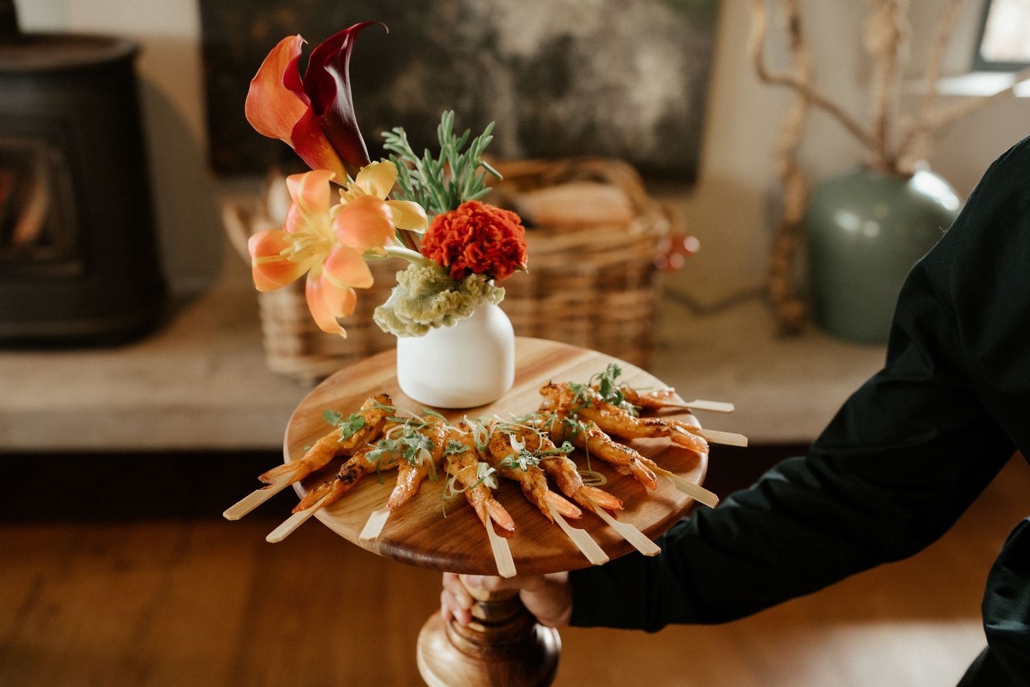 Elegant appetizer platter with red flowers displayed on wooden stand at wedding reception.
