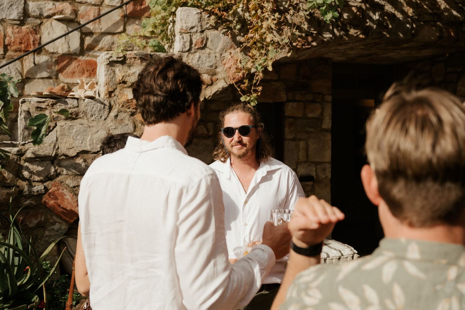 People gather together in conversation on a sunny day against a rustic stone wall background.