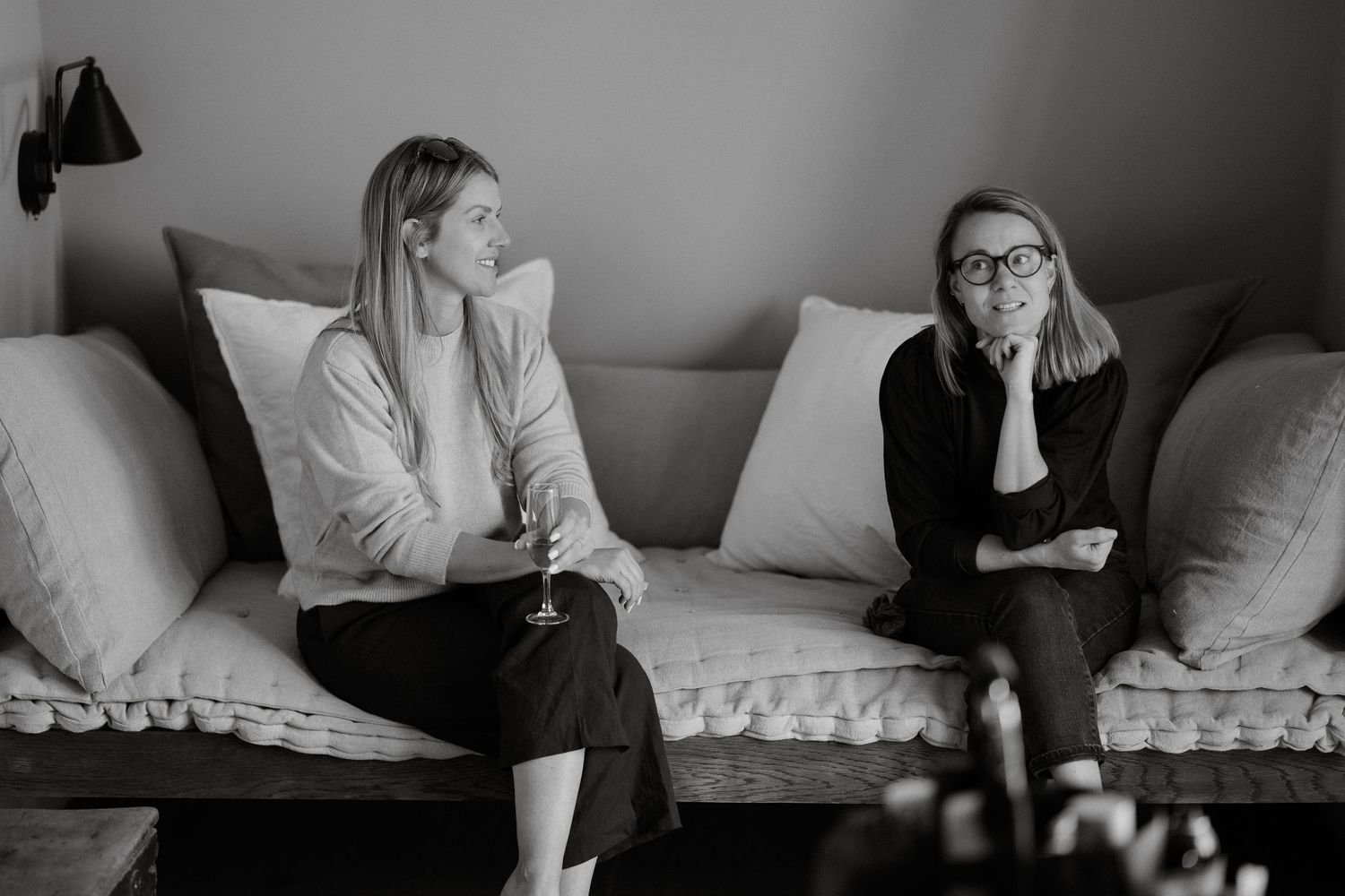 Two people sit together on a gray couch having a casual conversation in a minimalist living room.