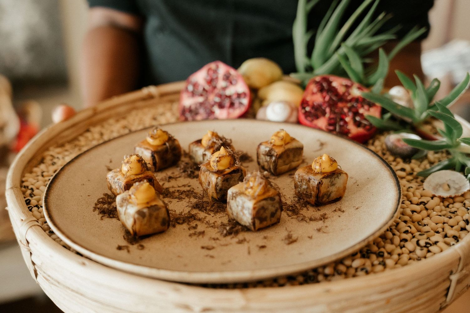 Golden appetizers with garnishes arranged on a decorative beige plate with a pomegranate in the background.