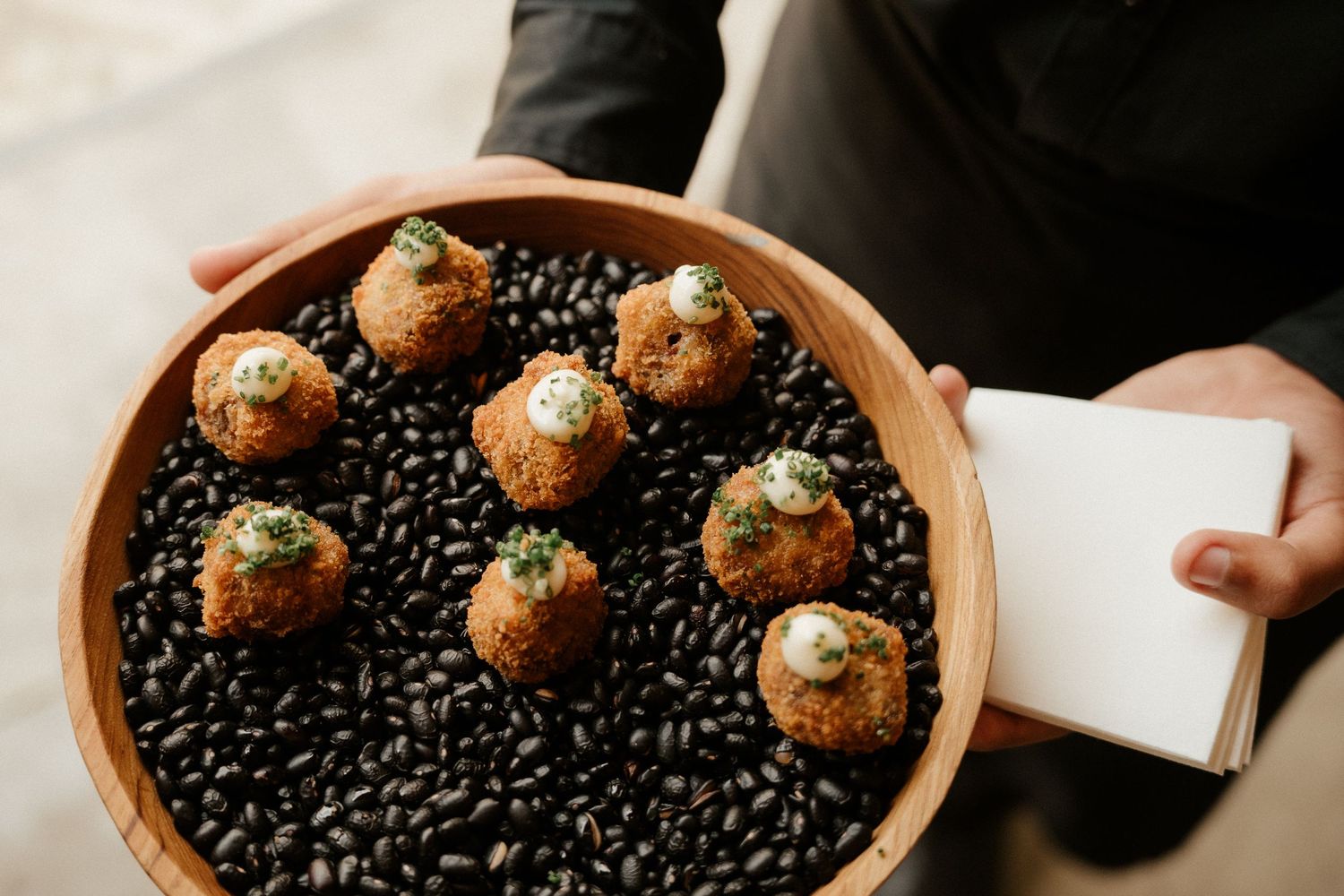 Crispy appetizer balls arranged on a bed of black beans in a rustic wooden bowl.