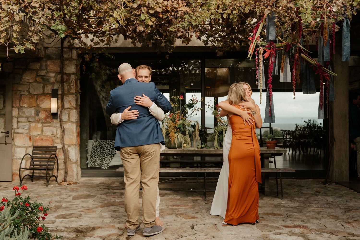 Wedding guests embrace and dance during an outdoor reception under floral decorations.