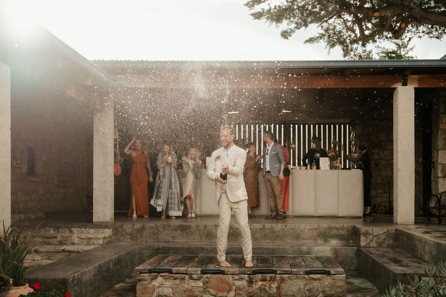 A reception scene at sunset with guests gathered on a stone patio.